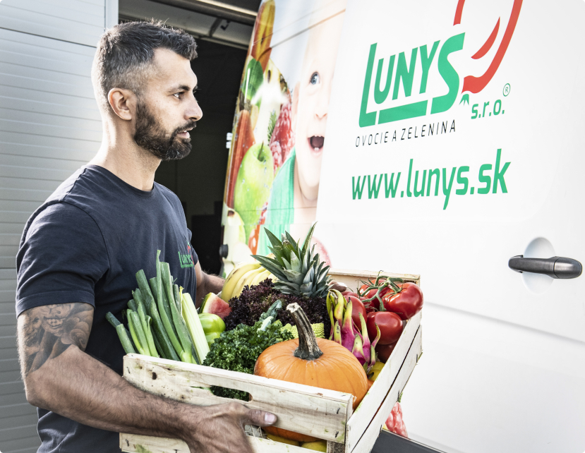Svalovec z Lunysu nakladá bedničku plnú ovocia a zeleninu do auta na prepravu